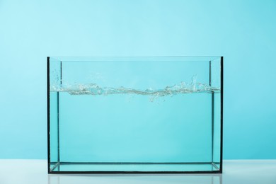 Photo of Glass aquarium with splashing water on table against light blue background