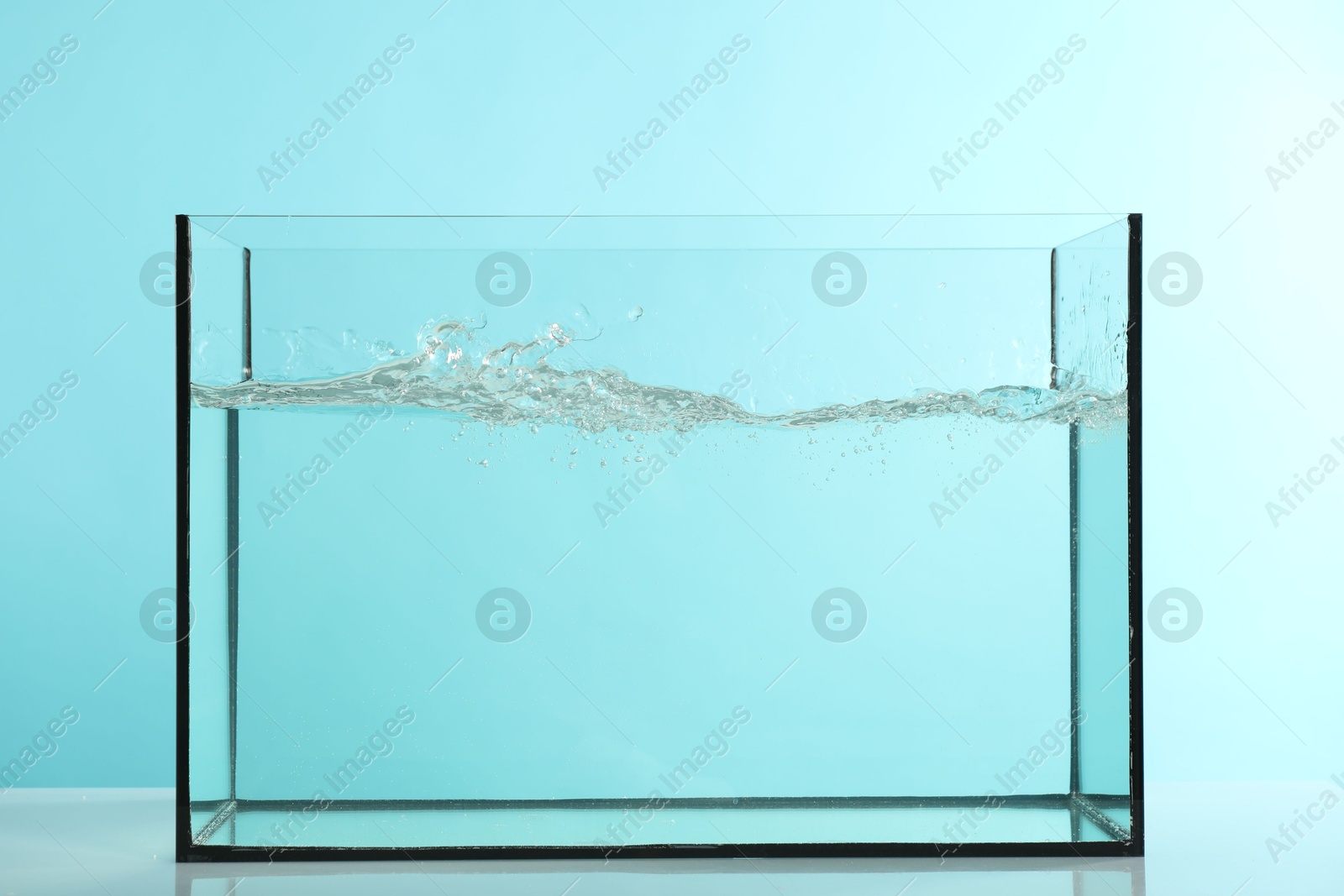 Glass aquarium with splashing water on table against light blue background Photo of Glass aquarium with splashing water on table against light blue background
