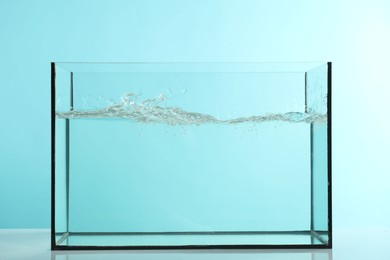 Photo of Glass aquarium with splashing water on table against light blue background