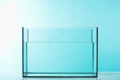 Photo of Glass aquarium with water on table against light blue background