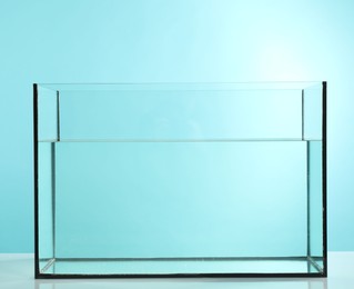 Photo of Glass aquarium with water on table against light blue background