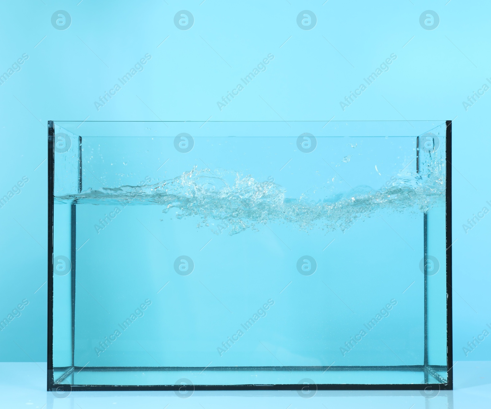 Glass aquarium with splashing water on table against light blue background Photo of Glass aquarium with splashing water on table against light blue background