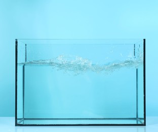 Photo of Glass aquarium with splashing water on table against light blue background