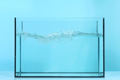 Photo of Glass aquarium with splashing water on table against light blue background