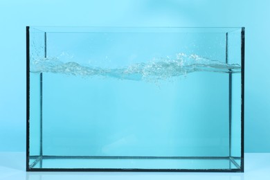 Photo of Glass aquarium with splashing water on table against light blue background