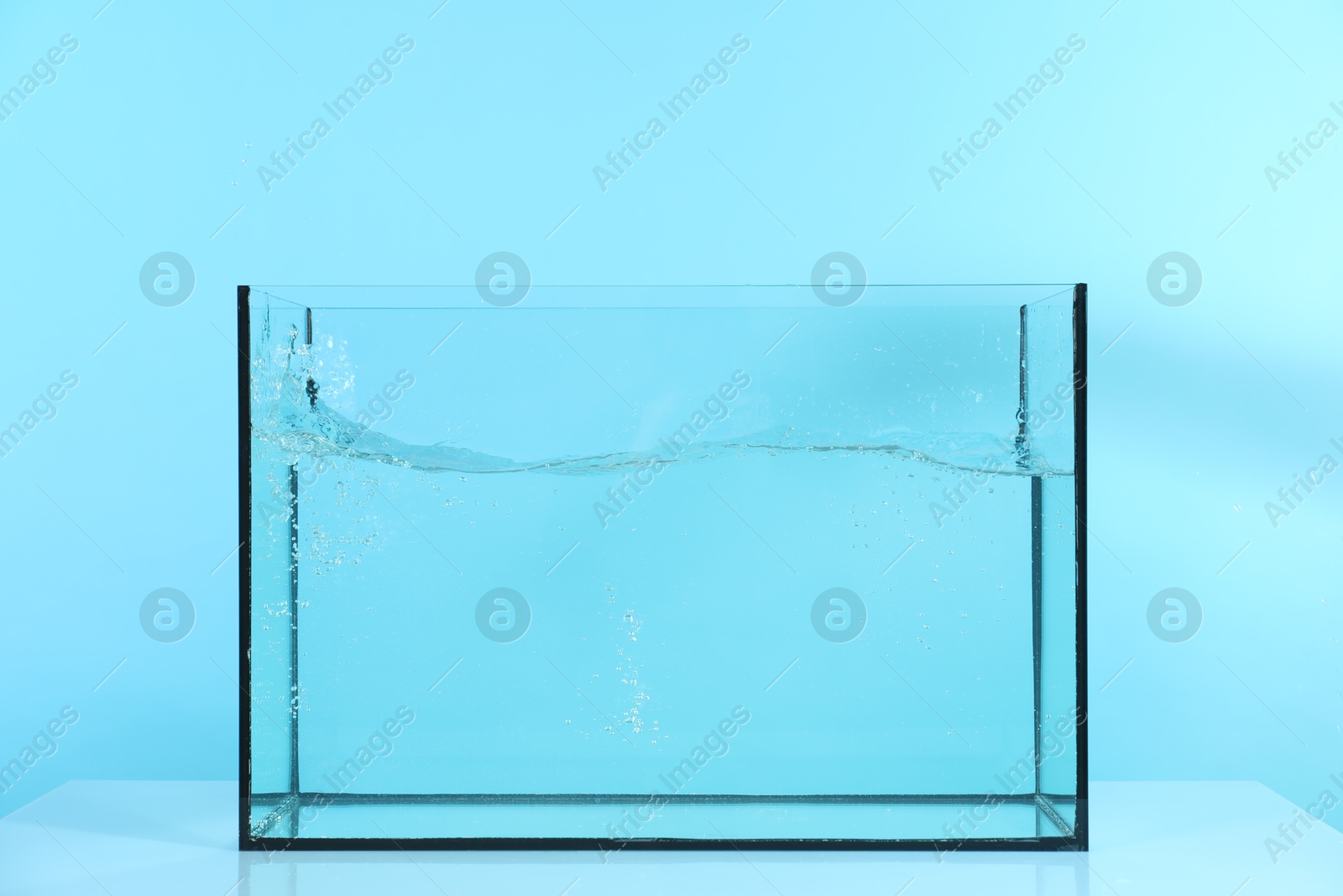 Glass aquarium with splashing water on table against light blue background Photo of Glass aquarium with splashing water on table against light blue background