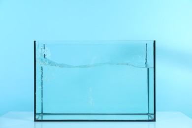 Photo of Glass aquarium with splashing water on table against light blue background