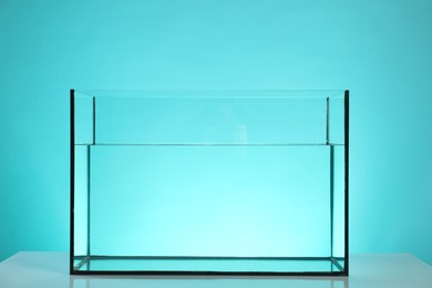 Photo of Glass aquarium with water on white table against turquoise background