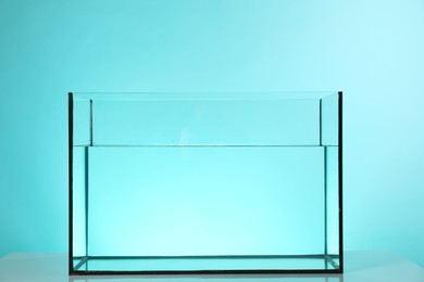 Photo of Glass aquarium with water on white table against turquoise background