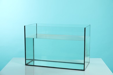 Photo of Glass aquarium with water on white table against turquoise background