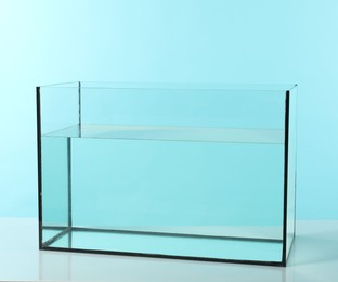 Photo of Glass aquarium with water on white table against turquoise background