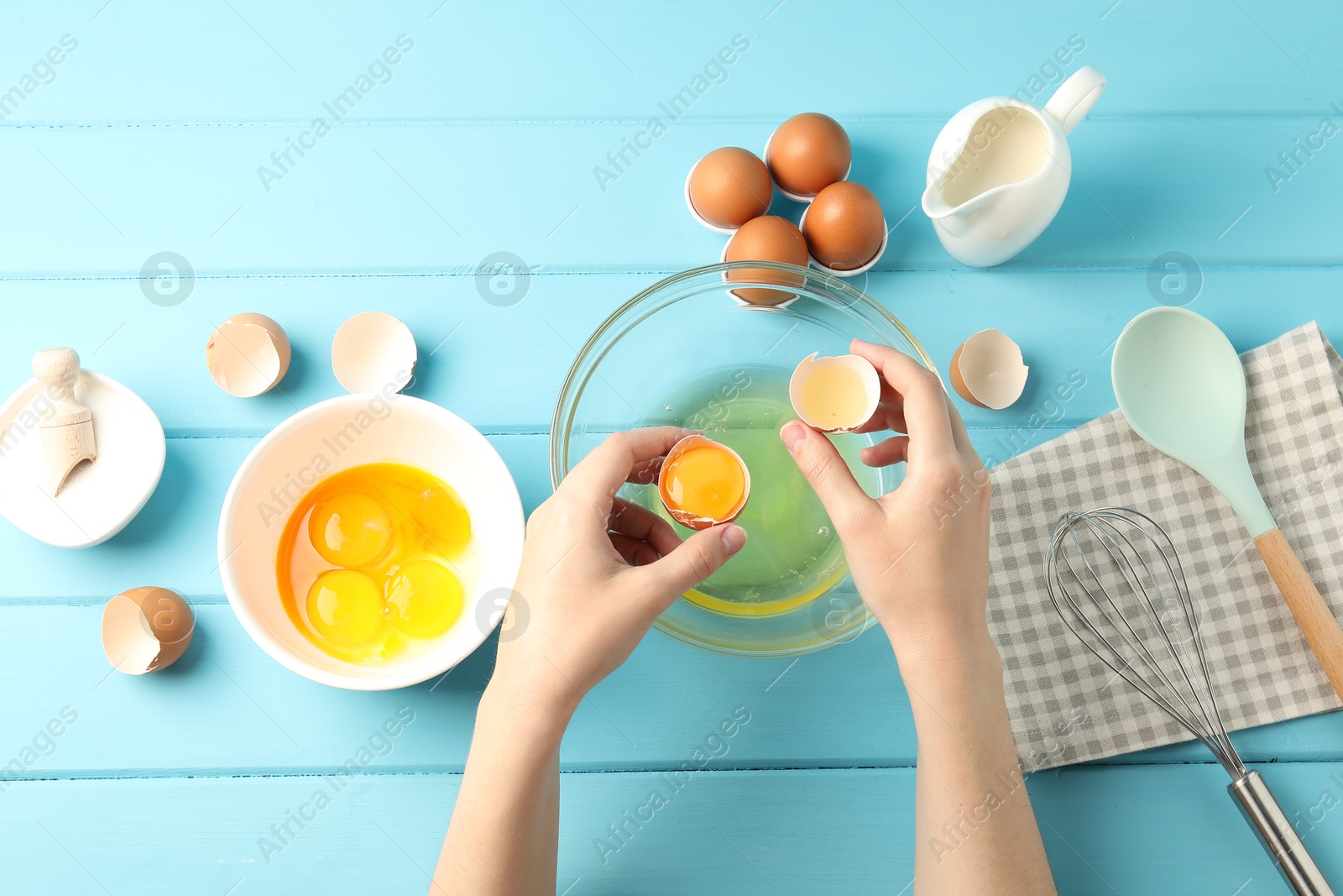 Woman separating egg yolk from white over glass bowl at light blue wooden table, top view Photo of Woman separating egg yolk from white over glass bowl at light blue wooden table, top view