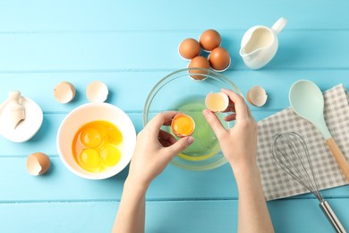 Photo of Woman separating egg yolk from white over glass bowl at light blue wooden table, top view