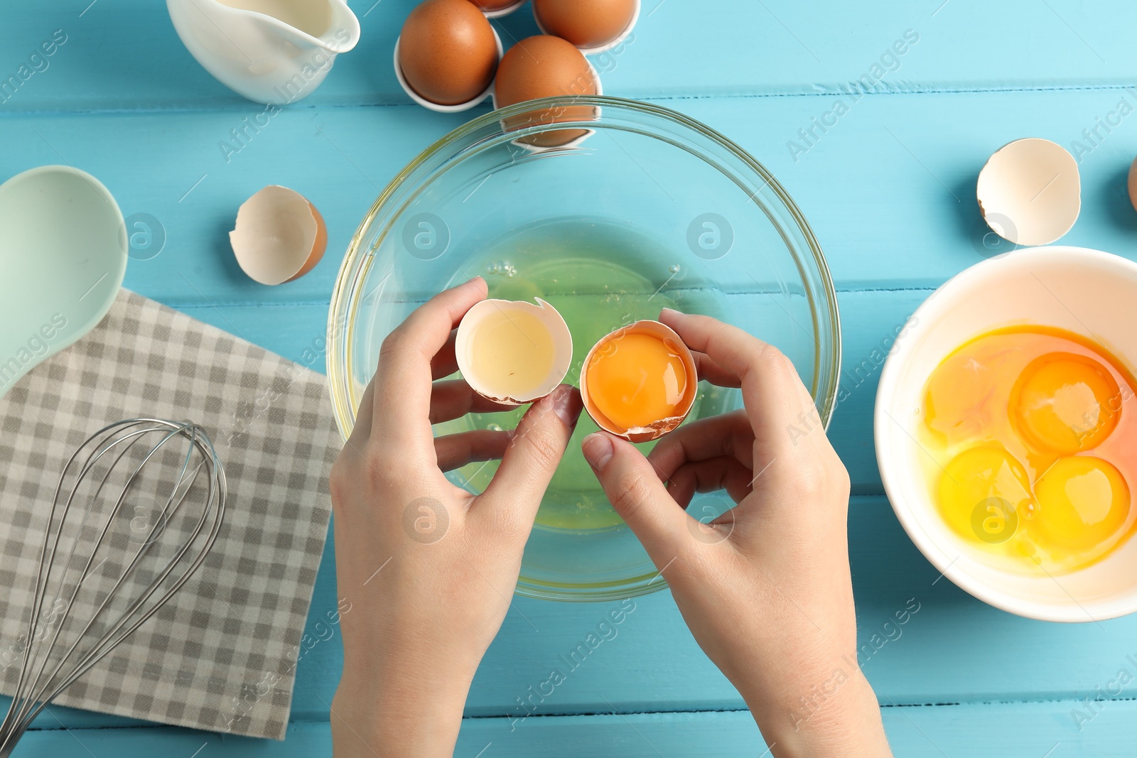 Woman separating egg yolk from white over glass bowl at light blue wooden table, top view Photo of Woman separating egg yolk from white over glass bowl at light blue wooden table, top view