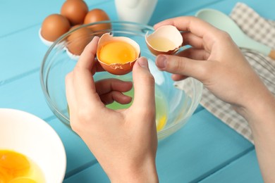 Photo of Woman separating egg yolk from white over glass bowl at light blue wooden table, closeup