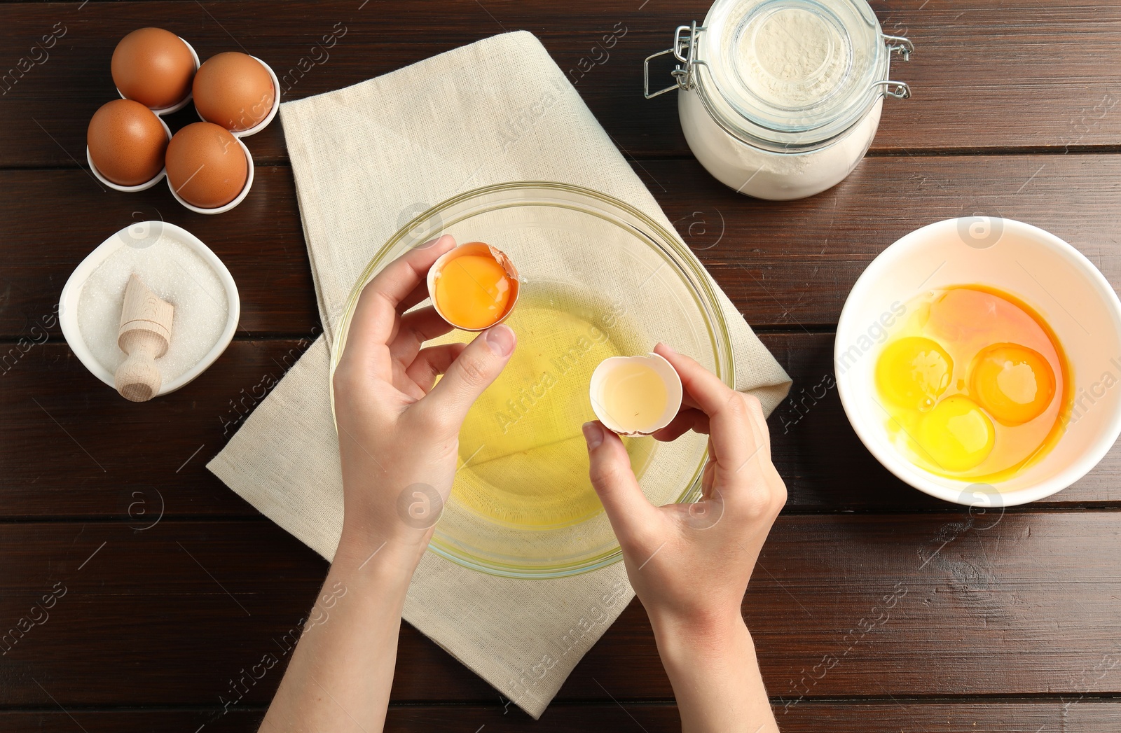 Woman separating egg yolk from white over glass bowl at wooden table, top view Photo of Woman separating egg yolk from white over glass bowl at wooden table, top view