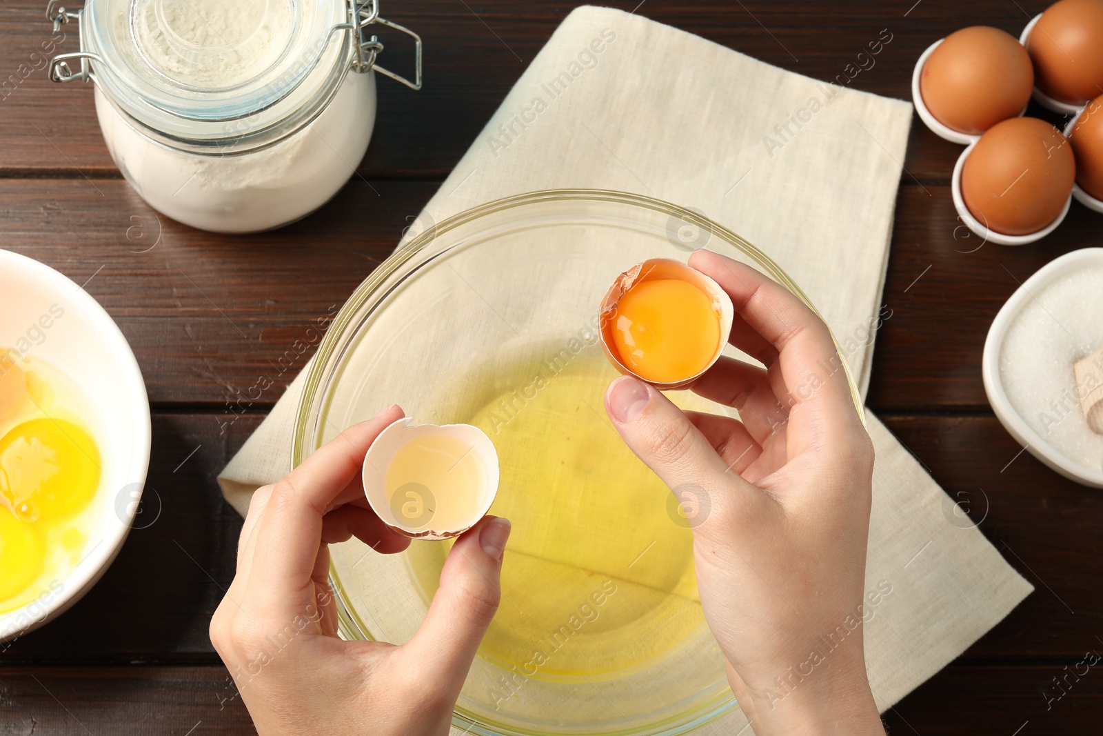 Woman separating egg yolk from white over glass bowl at wooden table, top view Photo of Woman separating egg yolk from white over glass bowl at wooden table, top view
