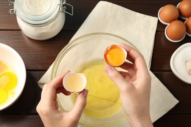 Photo of Woman separating egg yolk from white over glass bowl at wooden table, top view