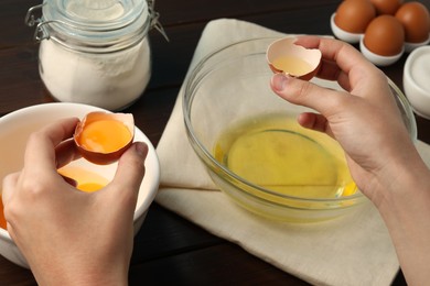 Photo of Woman separating egg yolk from white over glass bowl at table, closeup