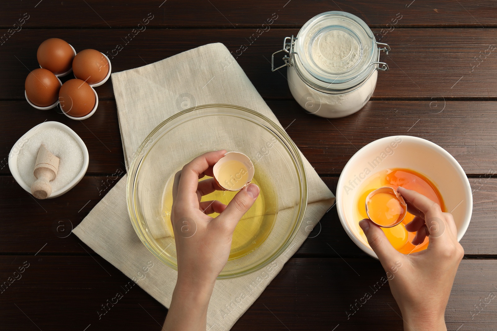 Woman separating egg yolk from white over glass bowl at wooden table, top view Photo of Woman separating egg yolk from white over glass bowl at wooden table, top view