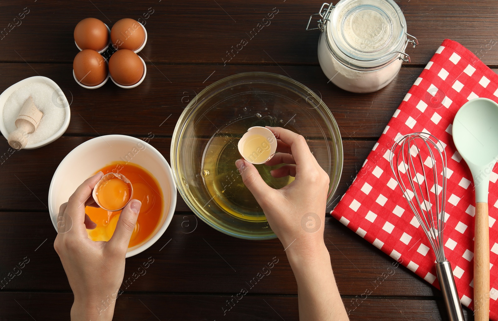 Woman separating egg yolk from white over glass bowl at wooden table, top view Photo of Woman separating egg yolk from white over glass bowl at wooden table, top view