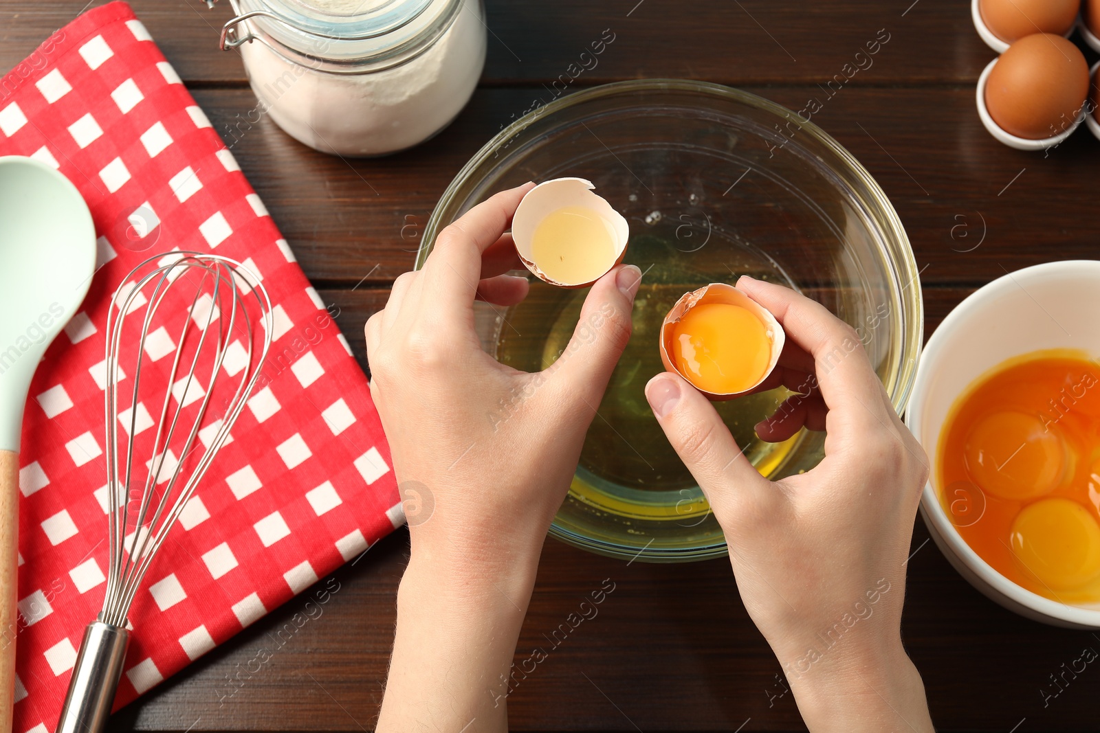 Woman separating egg yolk from white over glass bowl at wooden table, top view Photo of Woman separating egg yolk from white over glass bowl at wooden table, top view