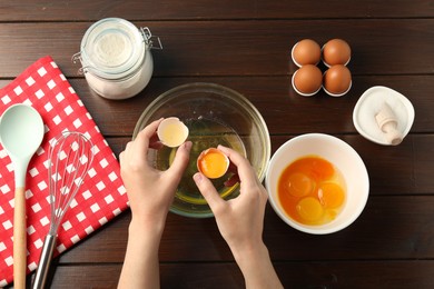 Photo of Woman separating egg yolk from white over glass bowl at wooden table, top view