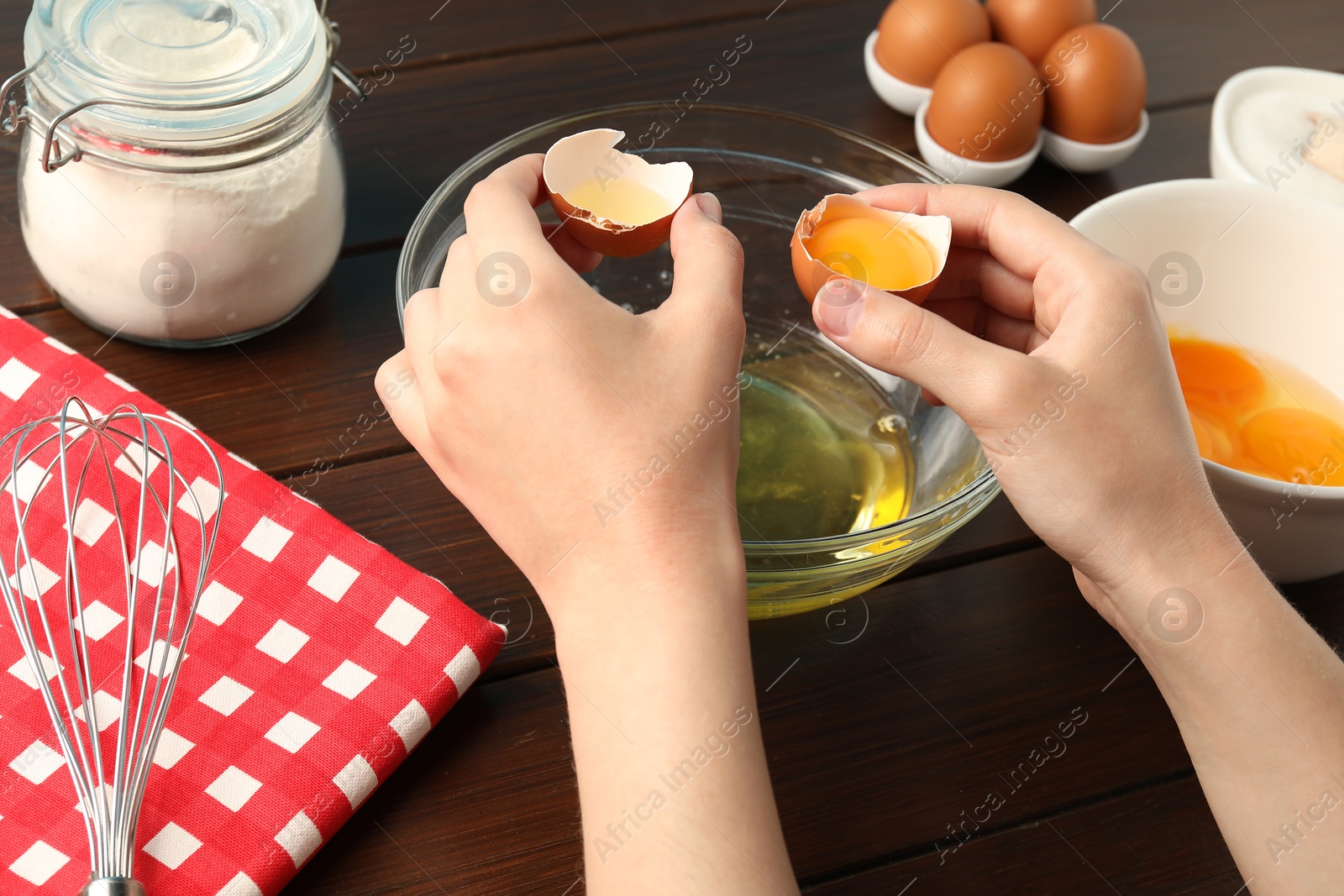 Woman separating egg yolk from white over glass bowl at wooden table, closeup Photo of Woman separating egg yolk from white over glass bowl at wooden table, closeup