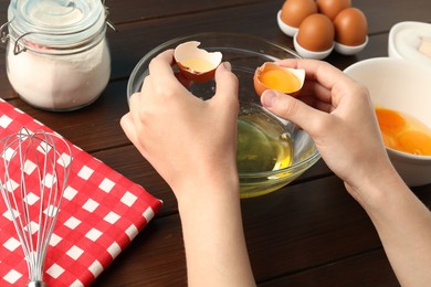 Photo of Woman separating egg yolk from white over glass bowl at wooden table, closeup