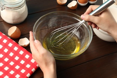 Photo of Woman whisking egg whites in bowl at wooden table, closeup