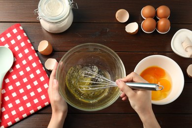 Photo of Woman whisking egg whites in bowl at wooden table, top view
