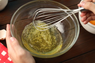 Photo of Woman whisking egg whites in bowl at wooden table, closeup