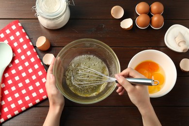 Photo of Woman whisking egg whites in bowl at wooden table, top view
