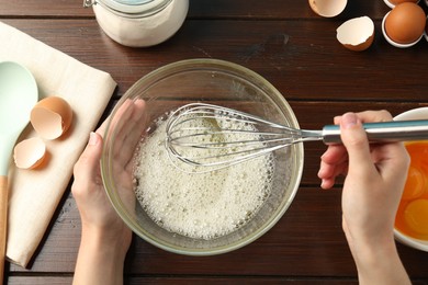 Photo of Woman whisking egg whites in bowl at wooden table, top view