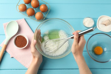 Photo of Woman whisking egg whites in bowl at light blue wooden table, top view
