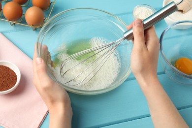 Photo of Woman whisking egg whites in bowl at light blue wooden table, closeup