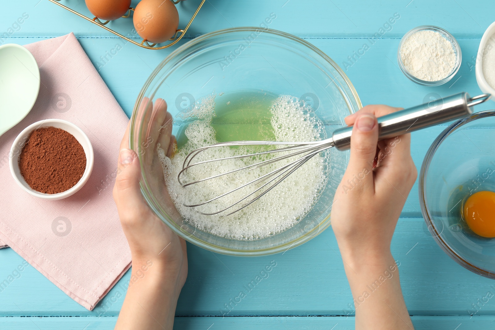 Woman whisking egg whites in bowl at light blue wooden table, top view Photo of Woman whisking egg whites in bowl at light blue wooden table, top view