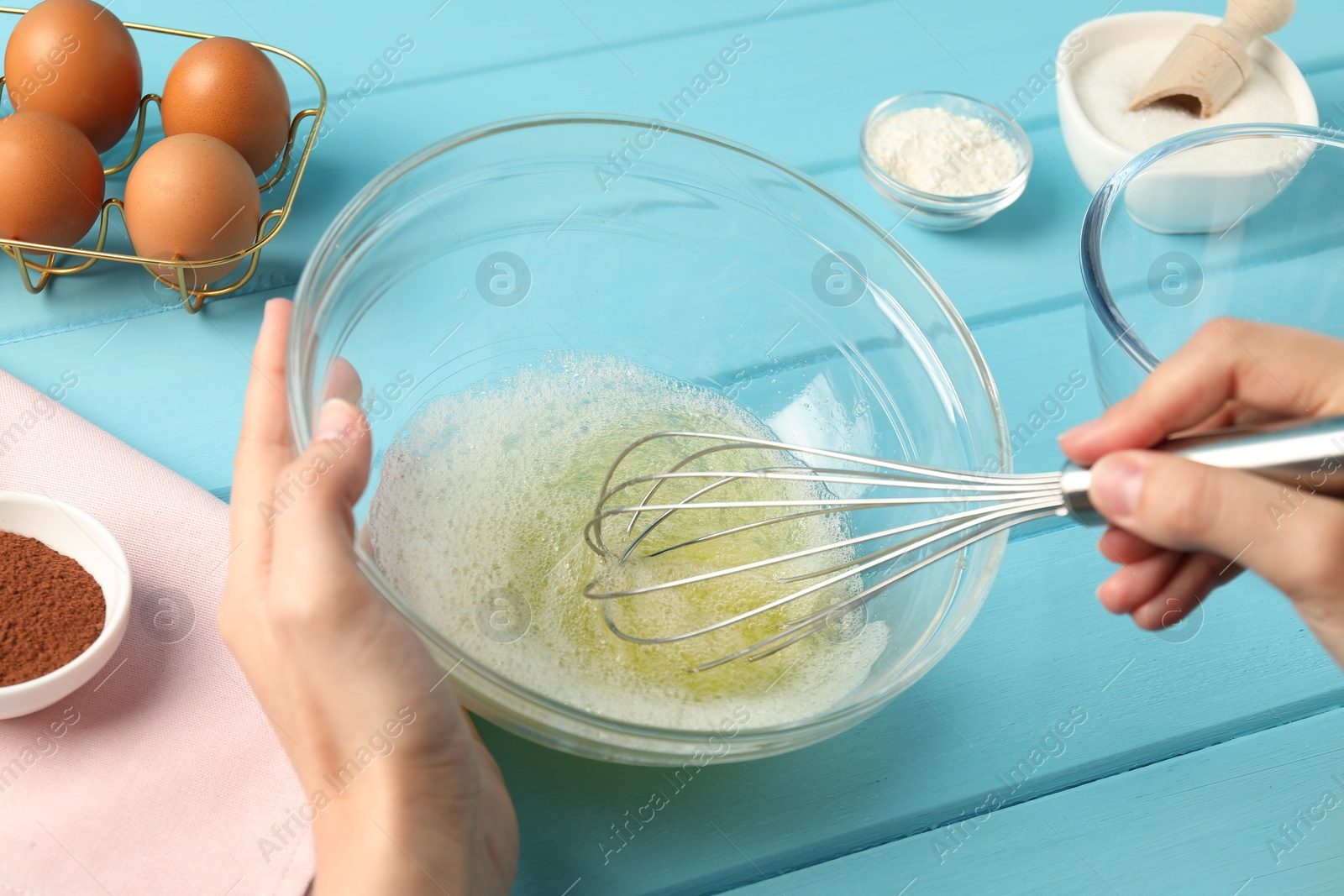 Woman whisking egg whites in bowl at light blue wooden table, closeup Photo of Woman whisking egg whites in bowl at light blue wooden table, closeup