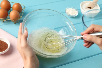 Photo of Woman whisking egg whites in bowl at light blue wooden table, closeup