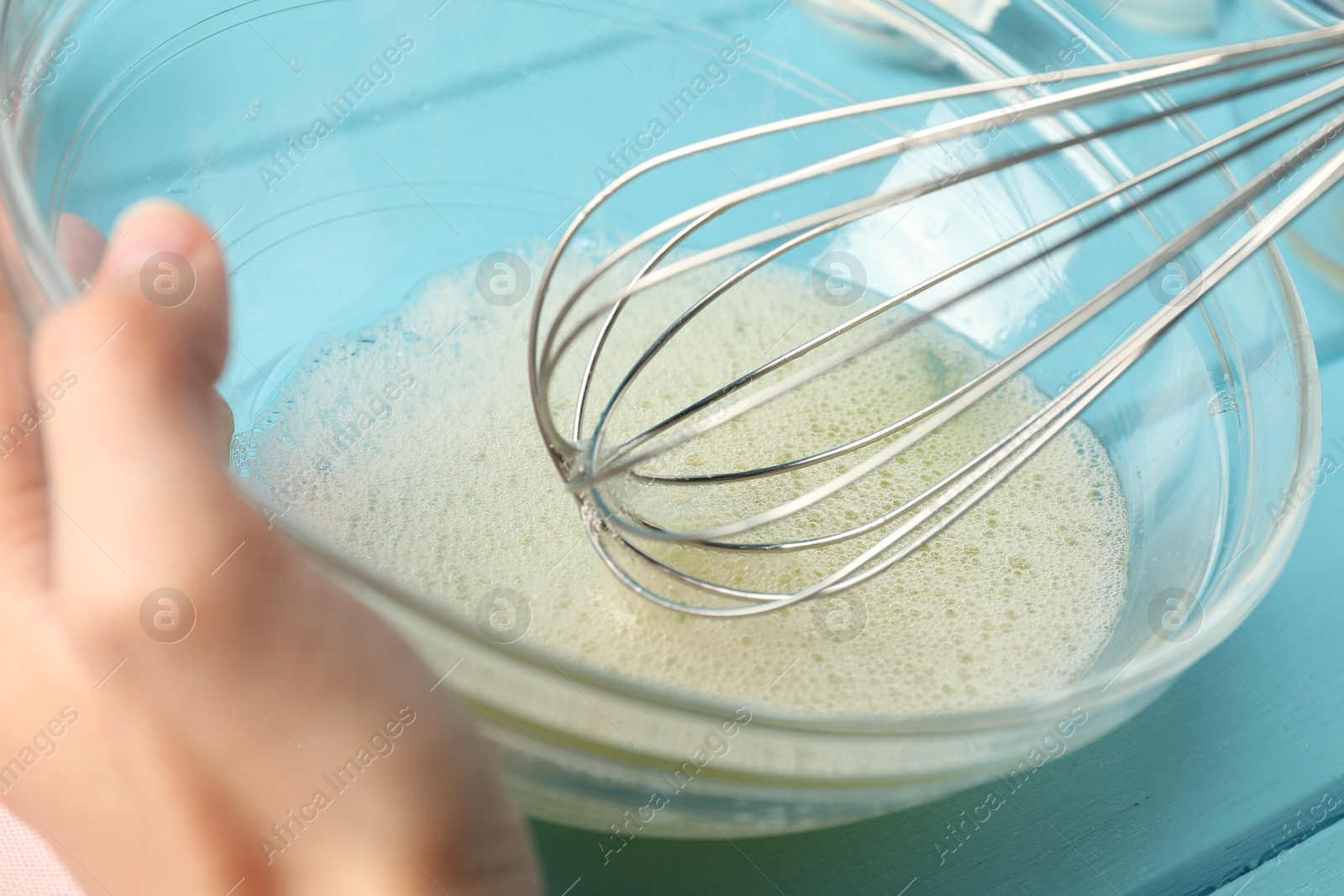 Woman whisking egg whites in bowl at light blue table, closeup Photo of Woman whisking egg whites in bowl at light blue table, closeup