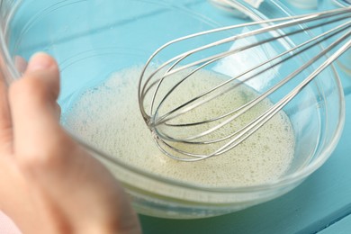 Photo of Woman whisking egg whites in bowl at light blue table, closeup