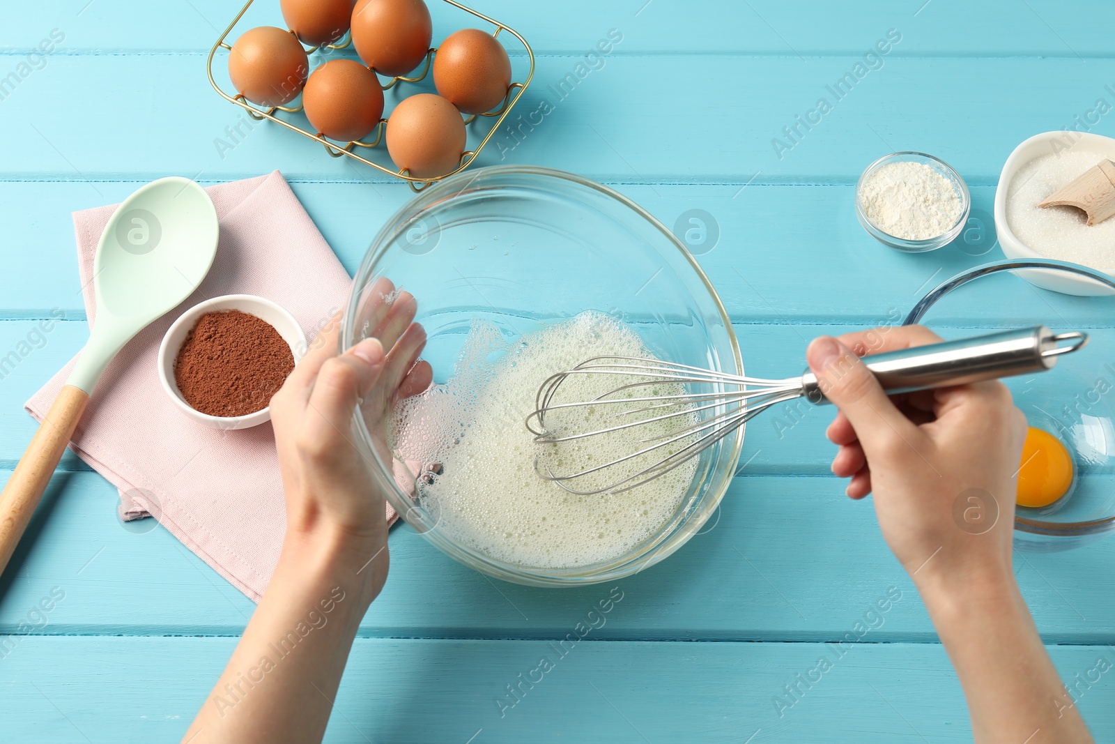 Woman whisking egg whites in bowl at light blue wooden table, top view Photo of Woman whisking egg whites in bowl at light blue wooden table, top view
