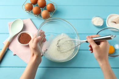 Photo of Woman whisking egg whites in bowl at light blue wooden table, top view