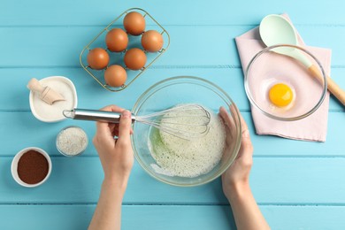 Photo of Woman whisking egg whites in bowl at light blue wooden table, top view
