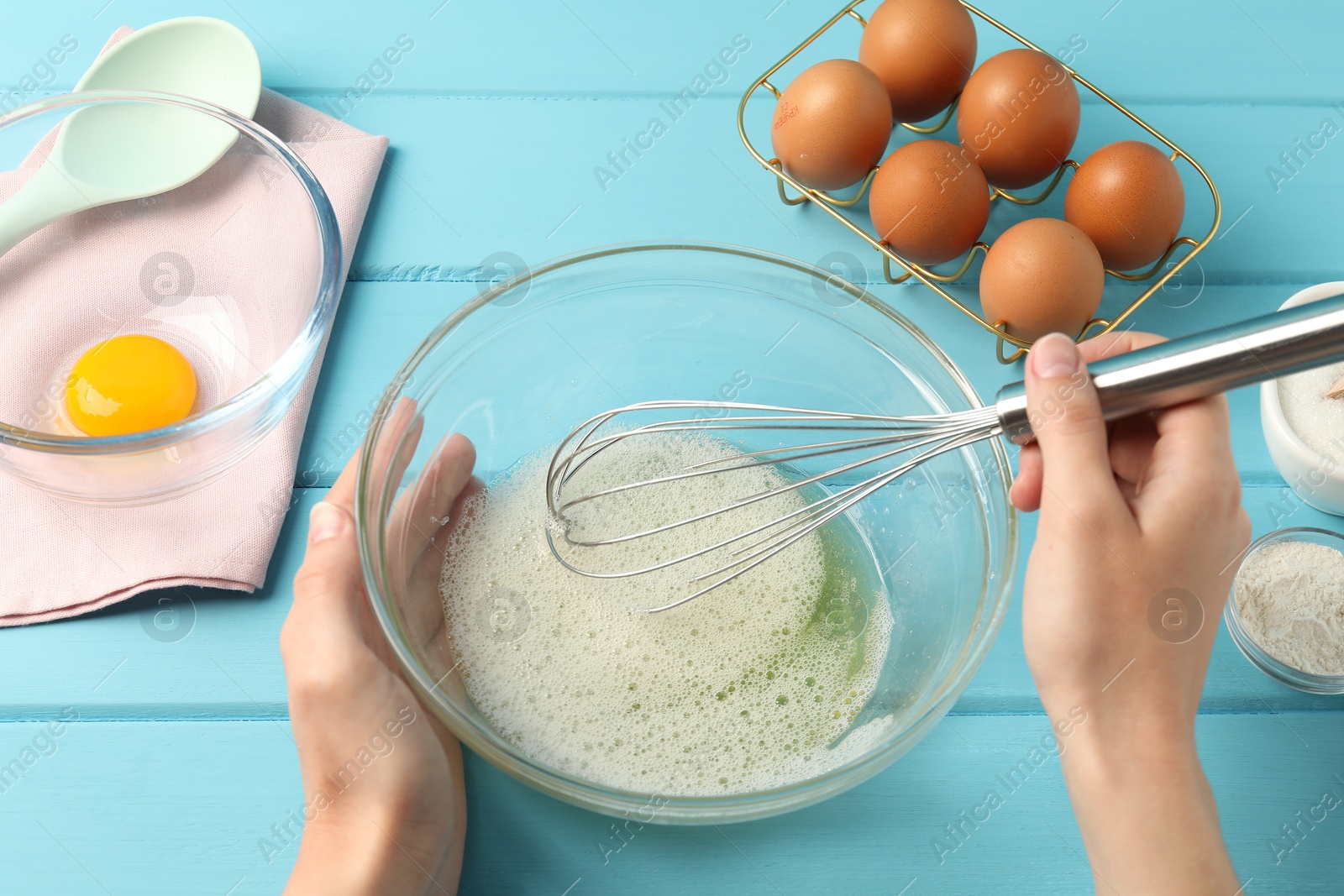 Woman whisking egg whites in bowl at light blue wooden table, above view Photo of Woman whisking egg whites in bowl at light blue wooden table, above view