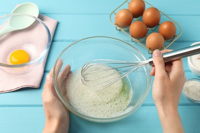 Photo of Woman whisking egg whites in bowl at light blue wooden table, above view