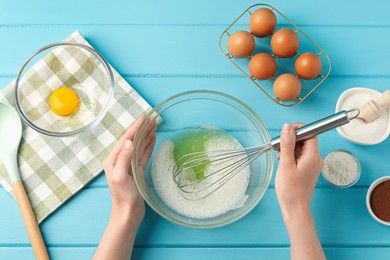 Photo of Woman whisking egg whites in bowl at light blue wooden table, top view