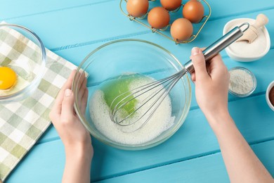 Photo of Woman whisking egg whites in bowl at light blue wooden table, above view