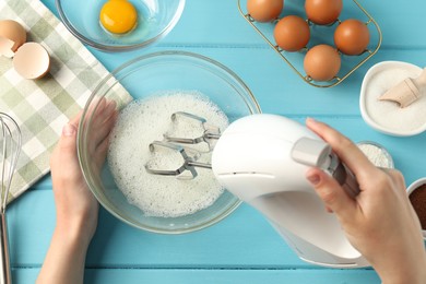 Photo of Woman whisking egg whites with hand mixer at light blue wooden table, top view