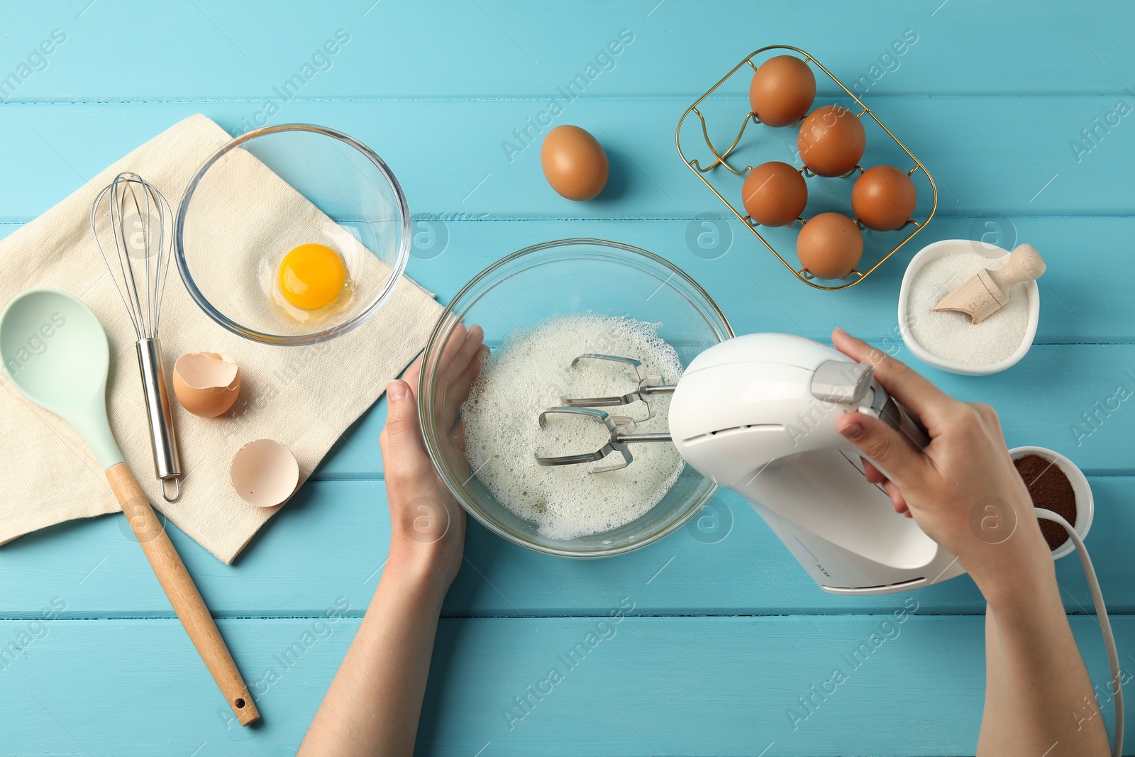 Woman whisking egg whites with hand mixer at light blue wooden table, top view Photo of Woman whisking egg whites with hand mixer at light blue wooden table, top view